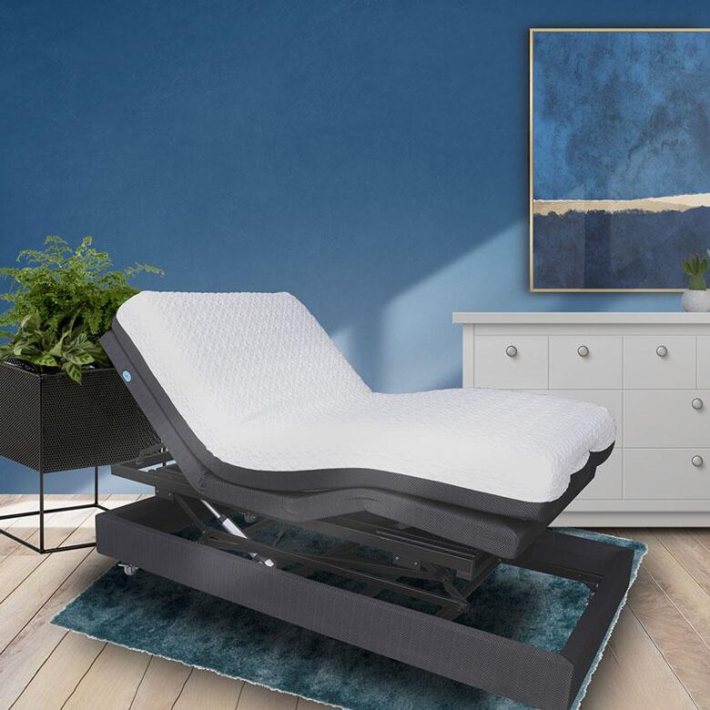 Image depicts an adjustable bed raised with the head of the bed sitting up in front of a blue wall and white dresser.